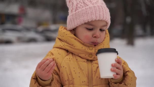 冬の雪の日に子供の女の子はココアを飲んで屋外でクッキーを食べる。幸せな子供時代の活動。クリスマス休暇だ。寒い天候 — ストック動画