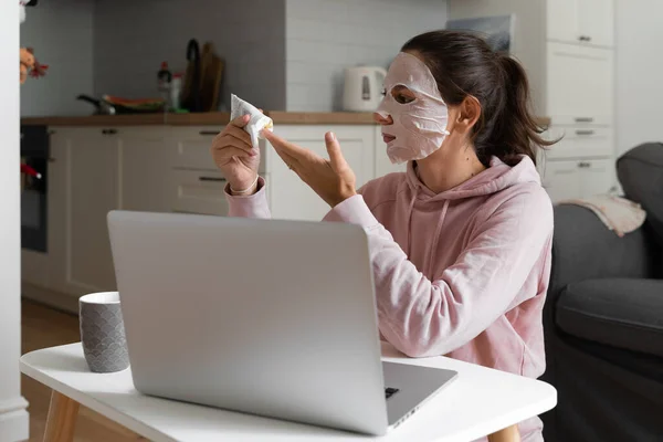 Jonge vrouw met schoonheidsmasker thuis. Snackable wellness concept. Zelfzorg voor het thuiskantoor. Snel gezichtsmasker voor thuis spa. — Stockfoto
