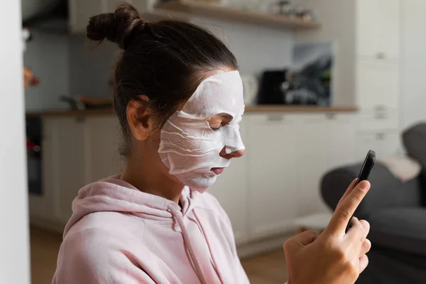 Mujer joven con máscara de belleza en casa. Concepto de bienestar merienda. Relajación en casa para una madre joven. Mascarilla facial rápida para spa en casa. — Foto de Stock