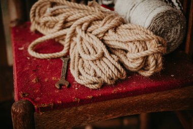 Garajında veya atölyesinde bordo döşemesi olan eski bir tahta sandalyenin arka planında beyaz ip ve ingiliz anahtarı.