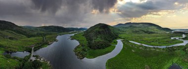 Güneş bulutların arasından parlarken Owengarriff Nehri ile Kerry İrlanda 'nın Killarney Ulusal Parkı' nda ön planda.