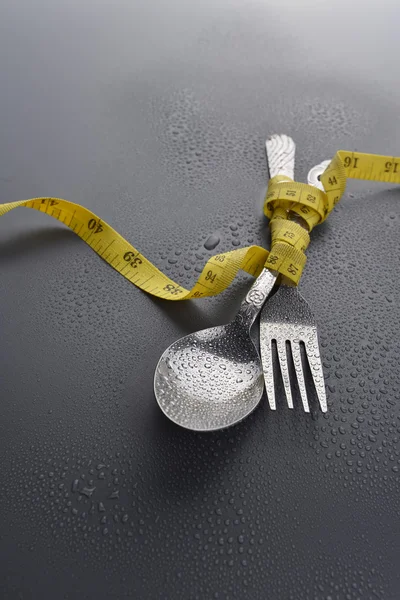 Chave de luz da colher, garfo e fita métrica amarela com gota de água no fundo cinza — Fotografia de Stock