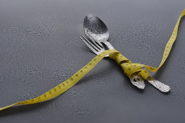 Lowlight key of spoon, fork and Yellow measuring tape with water drop on grey background — Stock Photo, Image