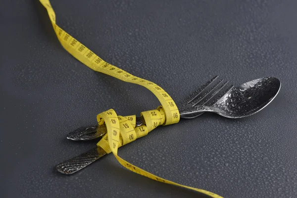 Lowlight key of spoon, fork and Yellow measuring tape with water drop on grey background — Stock Photo, Image