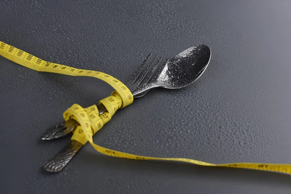 Clé basse de cuillère, fourchette et ruban à mesurer jaune avec goutte d'eau sur fond gris — Photo