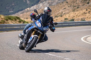 Profesyonel bir motosiklet sürücüsü yüksek hızda bir dağ yolu köşesine sıkıca yaslanıyor.