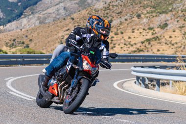 Profesyonel bir motosiklet sürücüsü yüksek hızda bir dağ yolu köşesine sıkıca yaslanıyor.