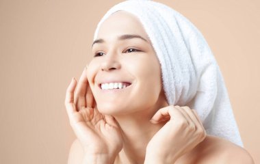 Bej arka planda saçında havlu olan tatlı bir kız. Temizleme, nemlendirme, yüz derisi için kurs.