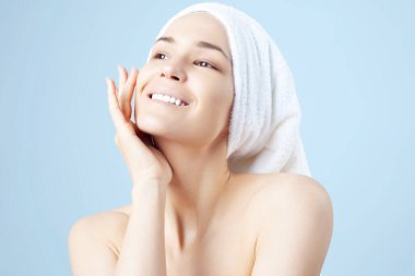 Mavi arka planda, saçında havlu olan tatlı, pozitif bir kız. Temizleme, nemlendirme, yüz derisi için kurs.