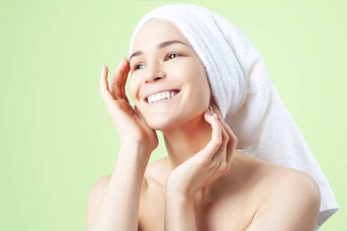 Yeşil arka planda saçında havlu olan tatlı pozitif bir kız. Temizleme, nemlendirme, yüz derisi için kurs.