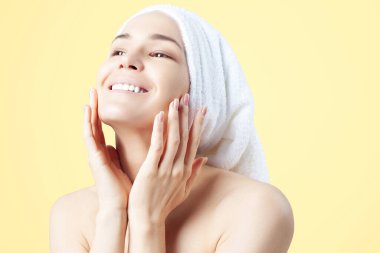 Saçında havlu olan tatlı, pozitif bir kız. sarı arka planda temizleme, nemlendirici, yüz derisi için rota