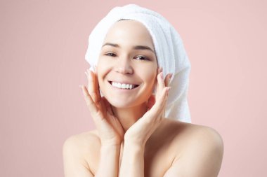 Pembe arka planda saçında havlu olan tatlı pozitif bir kız. Temizleme, nemlendirme, yüz derisi için kurs.