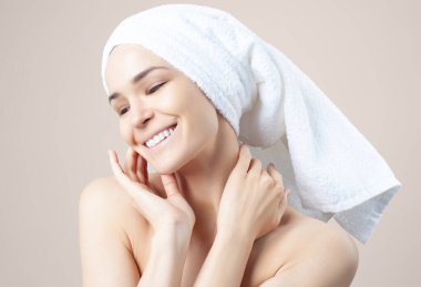 Bej arka planda saçında havlu olan tatlı bir kız. Temizleme, nemlendirme, yüz derisi için kurs.