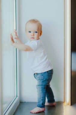 Küçük bebek pencerenin yanında duruyor. Çocuğun gelişimi, gelişimi ve öğrenimi