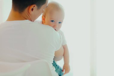 Küçük bebek babasının kollarında oturuyor. Çocuk bakımı ve babalık