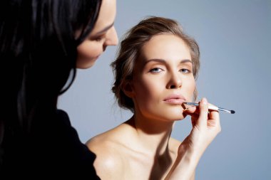 Güzel bir kadına doğal makyaj yapmak. Bir makyöz tarafından ruj düzeltmesi