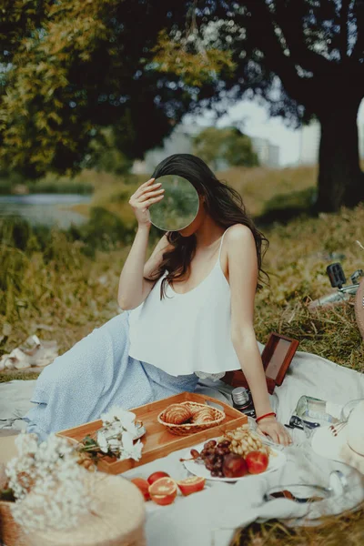 Beautiful young girl with mirror at picnic. Lifestyle, outdoor recreation on weekends