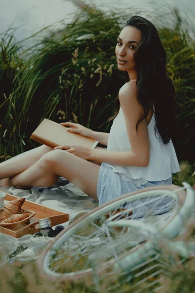 Beautiful young woman reads book at picnic. Lifestyle, outdoor recreation on weekends