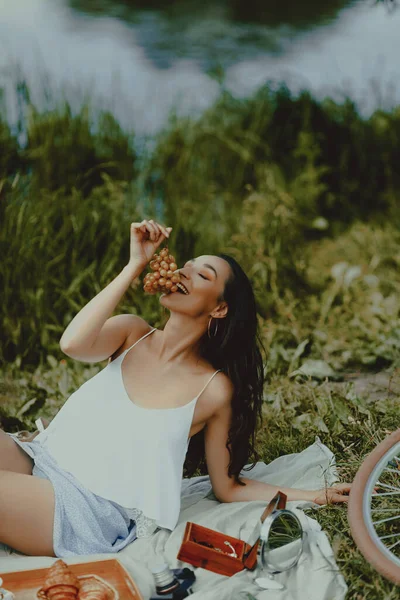 Beautiful playful woman eating grapes at picnic. Lifestyle, outdoor recreation on weekends