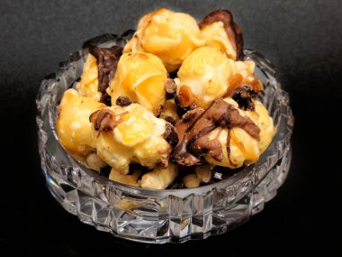 Koyu çikolata, deniz tuzu, karamelli patlamış mısır ve siyah arka planda mini kristal kase.