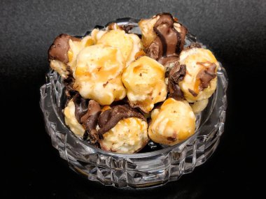 Koyu çikolata, deniz tuzu, karamelli patlamış mısır ve siyah arka planda mini kristal kase.