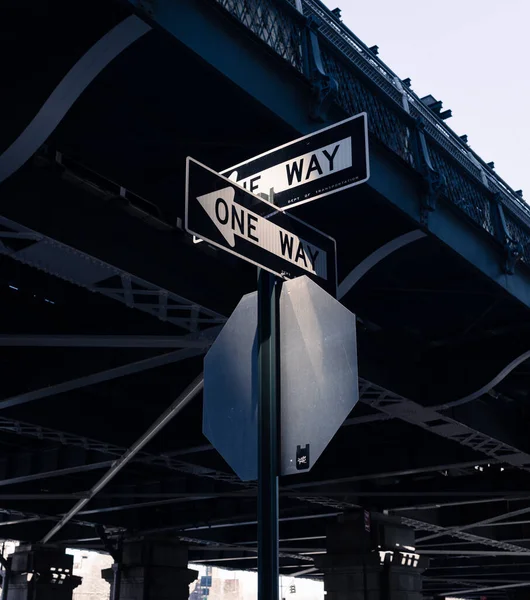 Two \'One Way\' signs intersecting under a bridge in dramatic light in New York City
