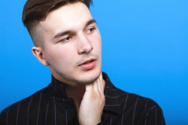 Modern saç stili olan genç yakışıklı bir adamın yakın portresi. Duygusal yüz, hafif sakal, siyah çizgili gömlek. Parlak mavi arkaplan, boşluğu kopyala.