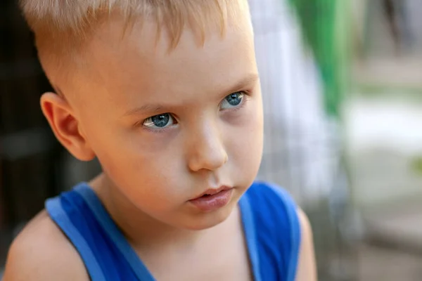 Close up portrait of beautiful baby boy with very serious look. Blond hair, blue eyes, strong emotions, sad face expression. Outdoors, copy space.