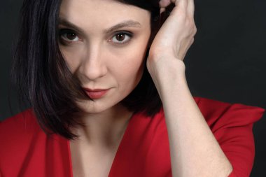 Çekici orta yaşlı kadın portresi, koyu renk saçlı ve gözleri olan, kameraya bakan, açık omuzlu kırmızı elbiseli. Egzotik görünüş, dumanlı makyaj. Siyah arkaplan.