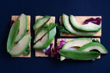 Avokado, yeşil bezelye ve salatalı vejetaryen tostları koyu lacivert arka planda. Boşluğu kopyala.