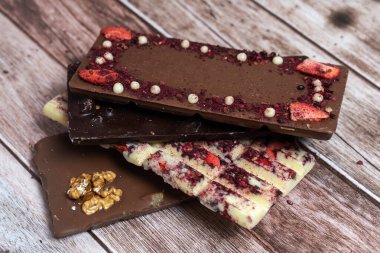 Eski ahşap arka planda farklı çikolata çeşitleri var. Siyah olan, süt ve beyaz, fındık, meyve ve böğürtlen parçaları. Çok lezzetliler. Aralığı Kopyala. 