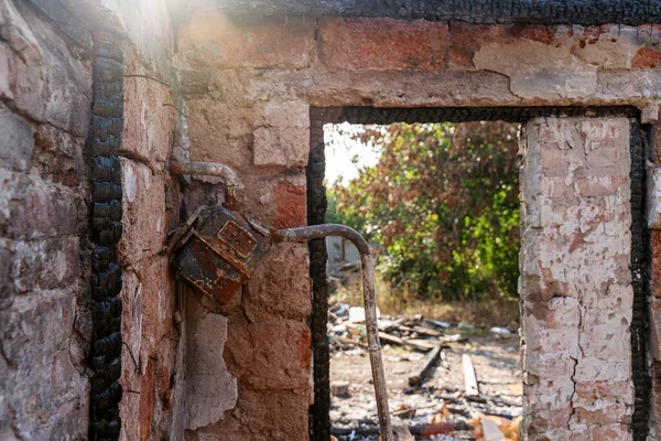 Ev yangınla yok oldu. Kayıp pencere, hasarlı gaz sayacı, yanmış ahşap çerçeve, çatlak duvarlar, harabeler. Güneş çatıdaki delikte parlıyor. 