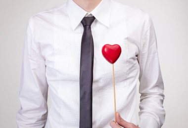 Beyaz gömlekli ve siyah kravatlı bir adam göğsünde küçük kırmızı bir kalp taşıyor. Duyguları, sevgiyi ya da desteği simgeliyor..