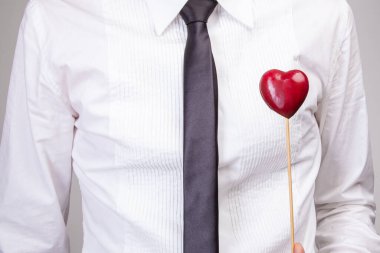 Portre çekici adam, kart kalp hediyesini gri arka planda izole edilmiş sıradan bir tişörtle tutuyor. Anneler Günü, Kadınlar Günü, Sevgililer Günü