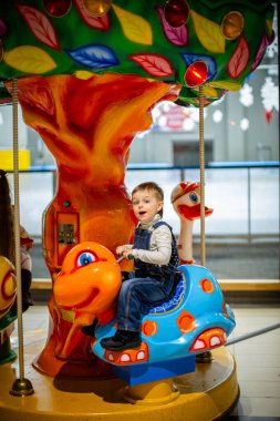 Alışveriş merkezinin eğlence alanında parlak dekorasyonları ve neşeli atmosferiyle renkli bir kaplumbağaya binen küçük çocuk..