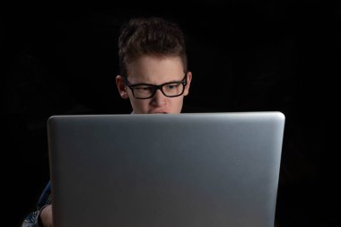 Gözlüklü ve gömlekli çocuk şüpheli bir şekilde dizüstü bilgisayarın arkasına bakıyor.