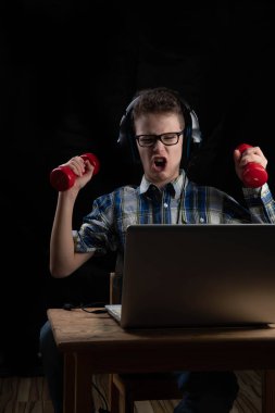 Evde eğitim görürken laptopun önünde iki dambılı olan genç bir erkek öğrenci.