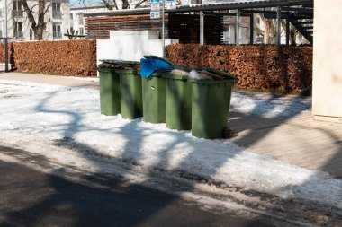 Kışın yol kenarındaki karda yeşil çöp tenekeleri