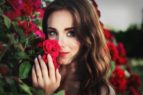 Portrait of a young brunette woman on a background of roses — Stock Photo, Image