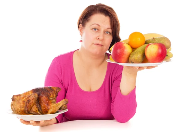 Uma mulher completa é a escolha do que comer frango ou frutas — Fotografia de Stock