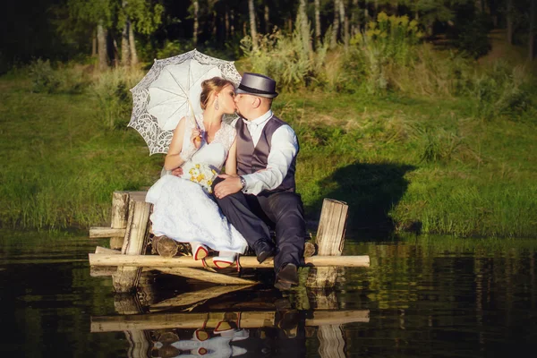 Beautiful bride and groom with umbrella on the bridge — Stock Photo, Image