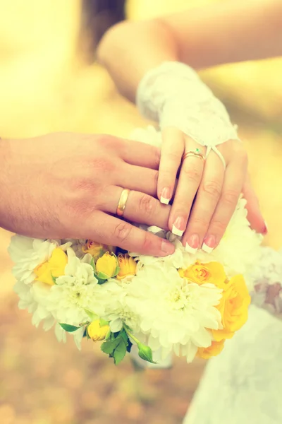 Bride and groom holding hands over bouquet — Stock Photo, Image