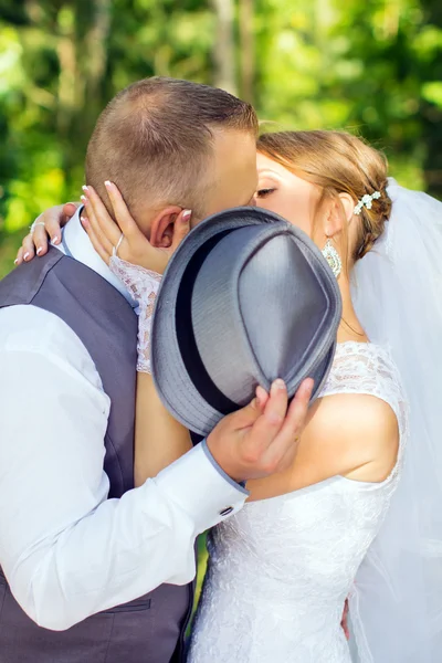 Bride and groom kissing hiding behind hat — Stock Photo, Image