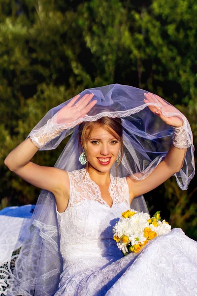 Bride sitting on the bridge with a bouquet — Stock Photo, Image