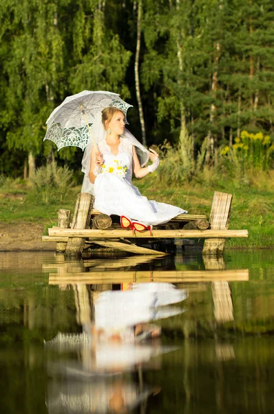 Sposa con ombrello seduta sul ponte — Foto Stock