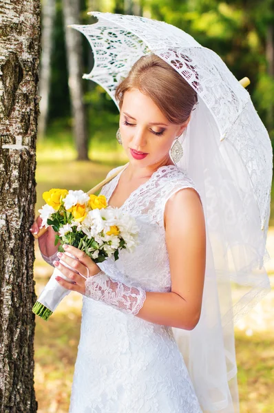 Beautiful young bride standing in the woods with umbrella — Stock Photo, Image