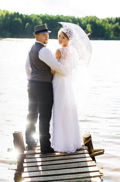 Bruid en bruidegom staande op een brug in de buurt van het water — Stockfoto