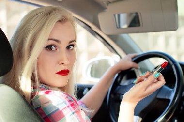 Güzel kız bir araba sürüş sırasında dudaklarını boyalar