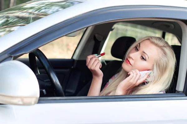 Chica pinta sus labios y hablar mientras conduce un coche — Foto de Stock