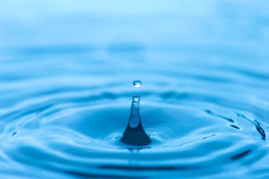 Su damlası damlayan ve yansıtan mavi renkli bir su damlası bardağa sıçrar..